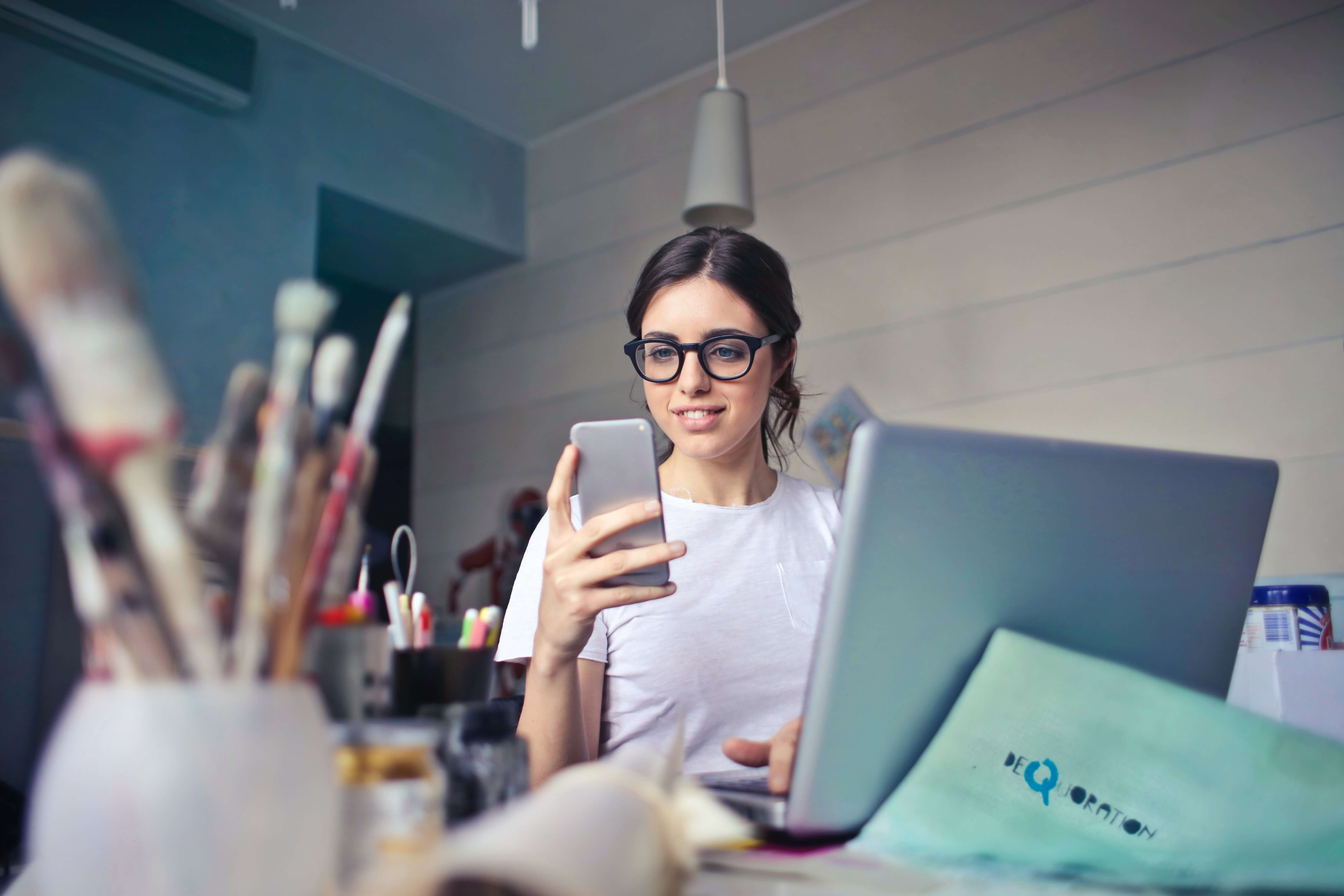 Woman at art desk in front of laptop booking Go Oil appointment on smartphone